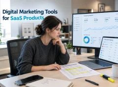 A marketer reviewing a list of software subscriptions on a laptop beside an annotated printed spreadsheet and an analytics dashboard.