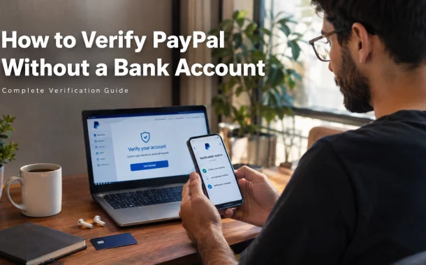 Young man at a modern home office desk holding a smartphone displaying a PayPal-style account verification screen, with a laptop showing an account verification page beside him. Desk holds a notebook, pen, debit card, wireless earbuds, and coffee cup. Soft natural light, clean minimalist setting. Overlay text: “How to Verify PayPal Without a Bank Account – Complete Verification Guide”.