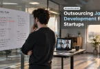 A startup founder reviewing an annotated hiring plan beside a laptop showing a video call with a distributed development team.
